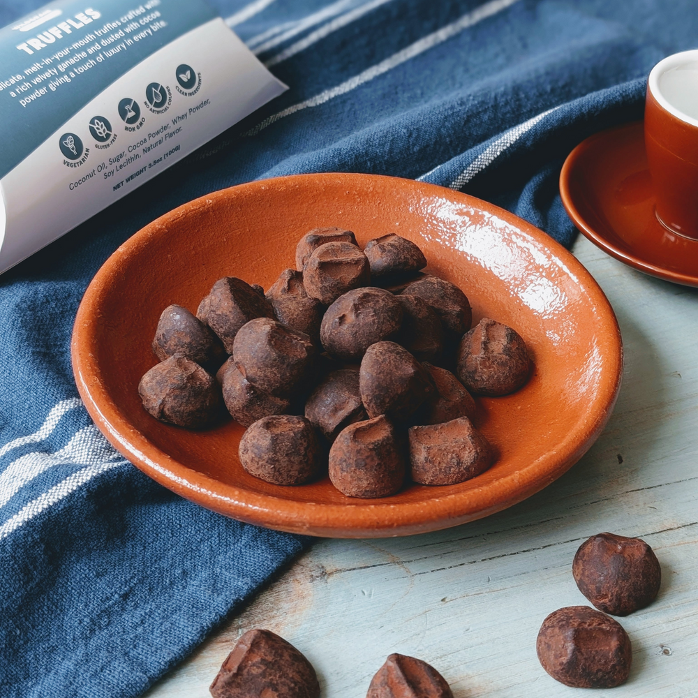 Chocolate truffles in an orange bowl on a blue cloth with a cup and saucer in the background.