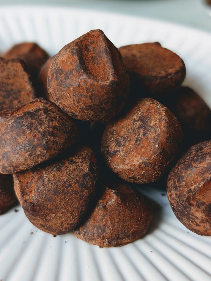 Chocolate truffles dusted with cocoa powder piled on a white ridged plate