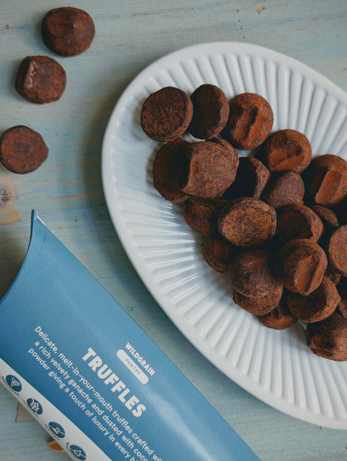 Cocoa-dusted chocolate truffles on a white plate beside blue package labeled WILDGRAIN PANTRY TRUFFLES.