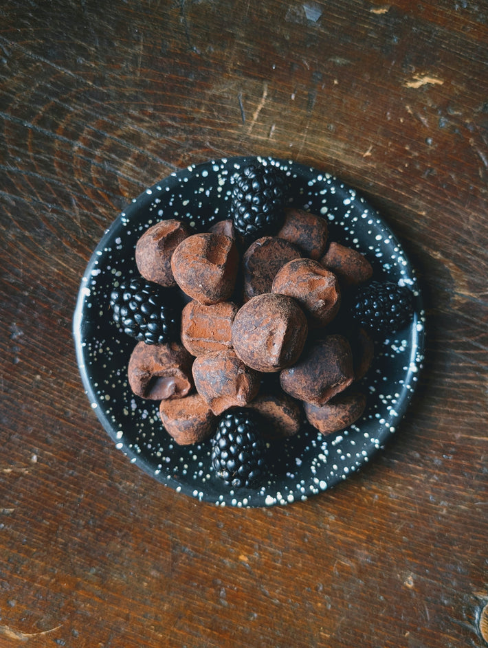Black cocoa-dusted chocolate truffles and blackberries on a speckled black plate, overhead view.