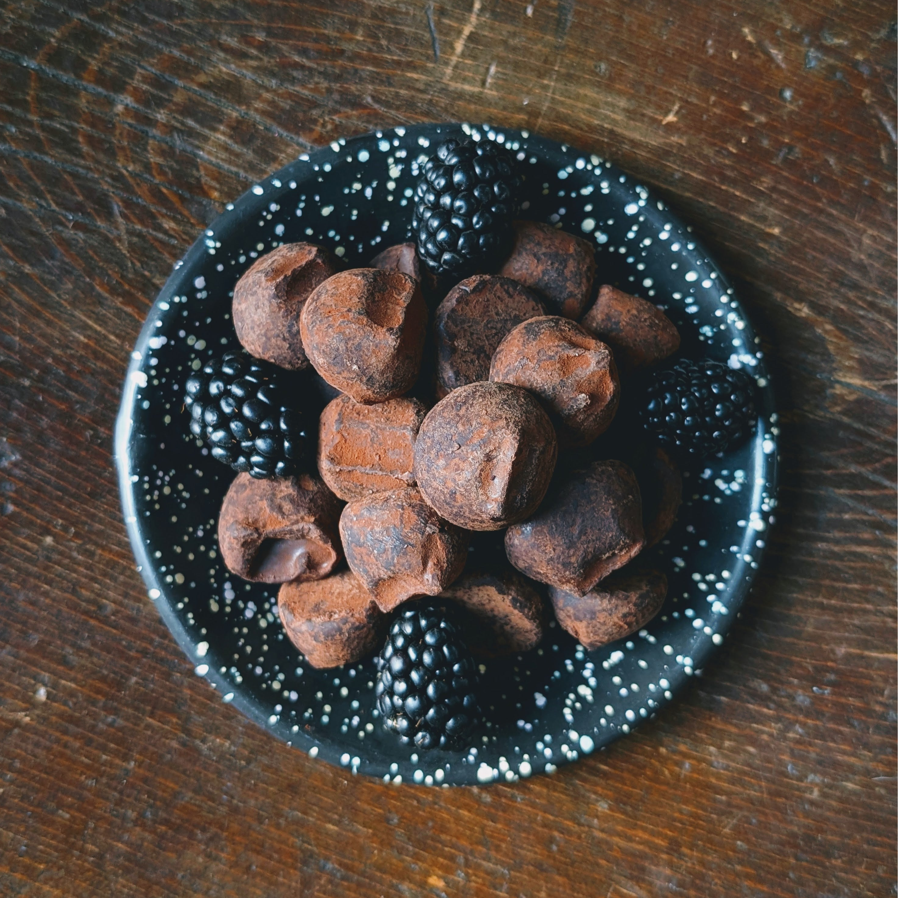 Dark chocolate truffles in a black speckled bowl on a wooden surface