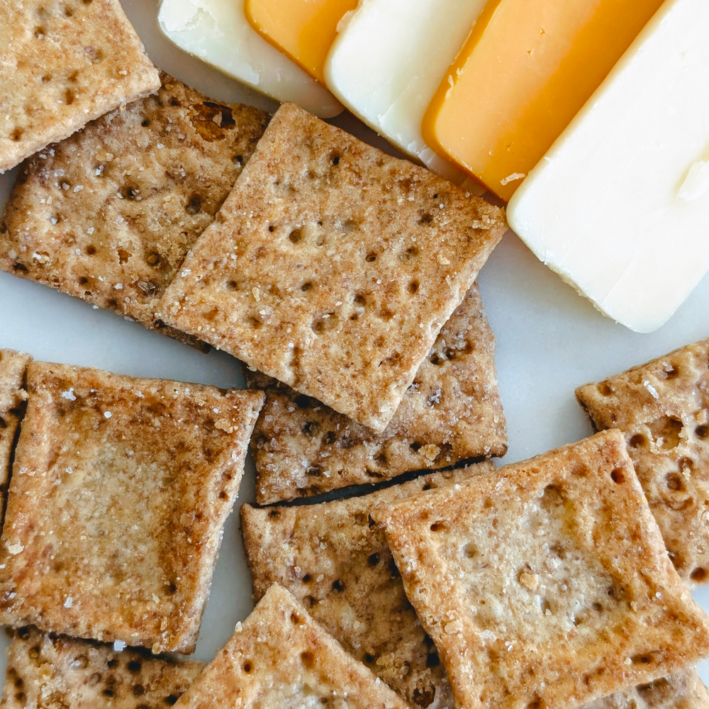 Crispy square crackers sprinkled with salt beside sliced orange cheddar and white cheese.
