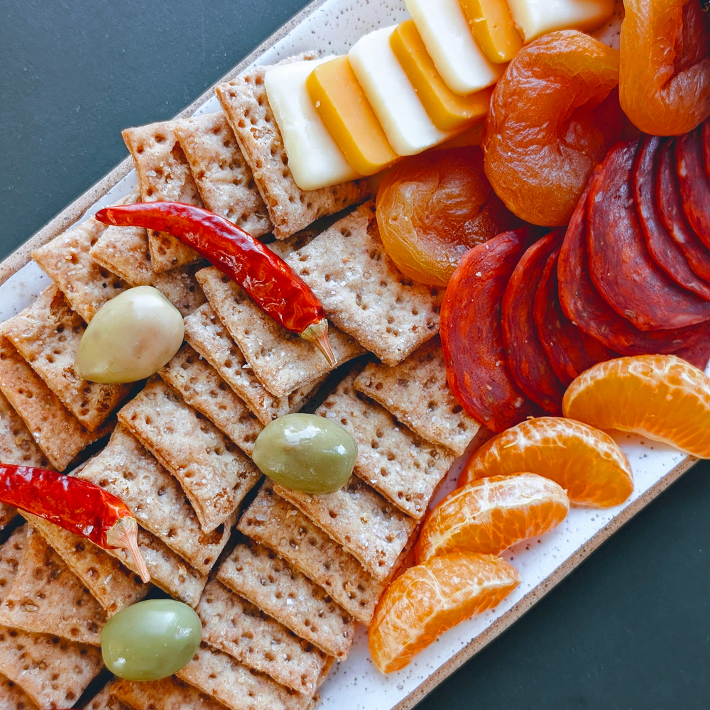 Charcuterie platter: crackers, green olives, red chilies, dried apricots, sliced cured sausage, cheese, tangerine wedges
