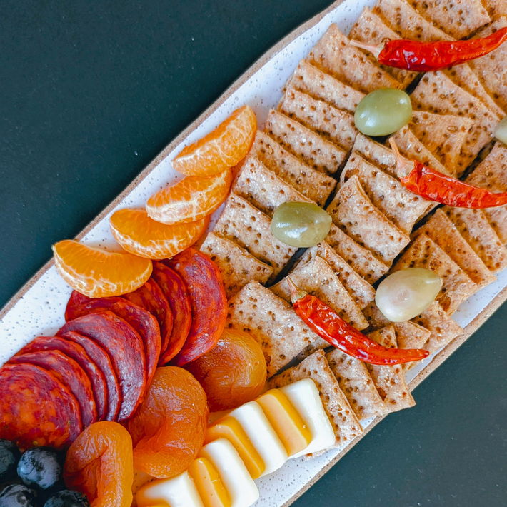 Platter of crackers with olives and chilies, sliced salami, dried apricots, mandarin wedges and sliced cheese.