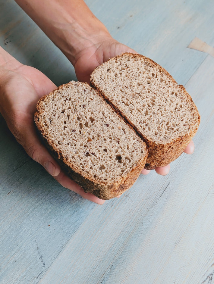 Gluten-Free Sourdough Loaf, cut in half to show the textured interior, against a light blue background.