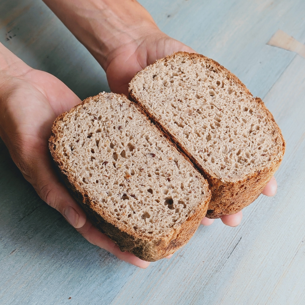 A person holding a halved Gluten-Free Sourdough Loaf, showing its airy crumb and texture.