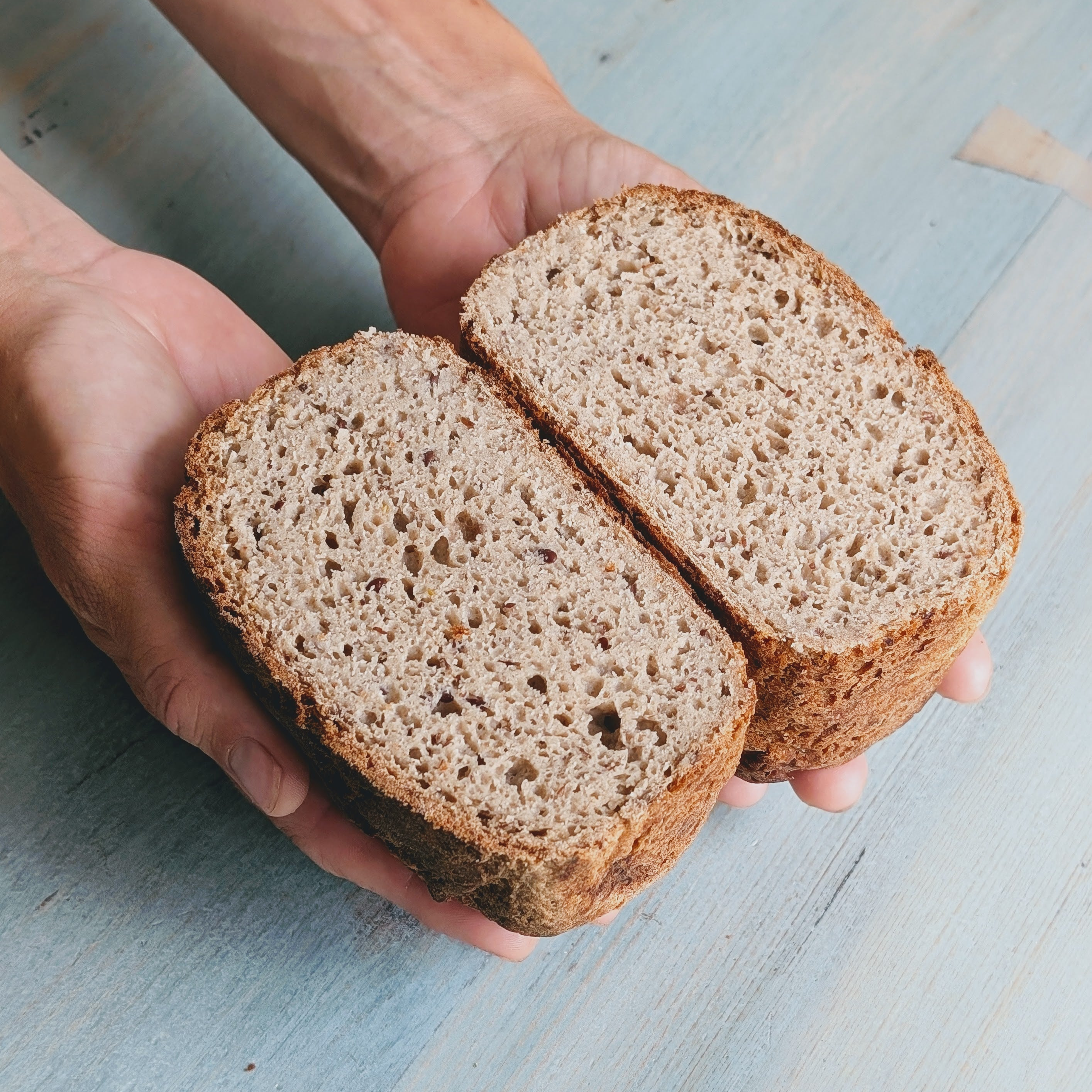 A person holding a halved Gluten-Free Sourdough Loaf, showing its airy crumb and texture.