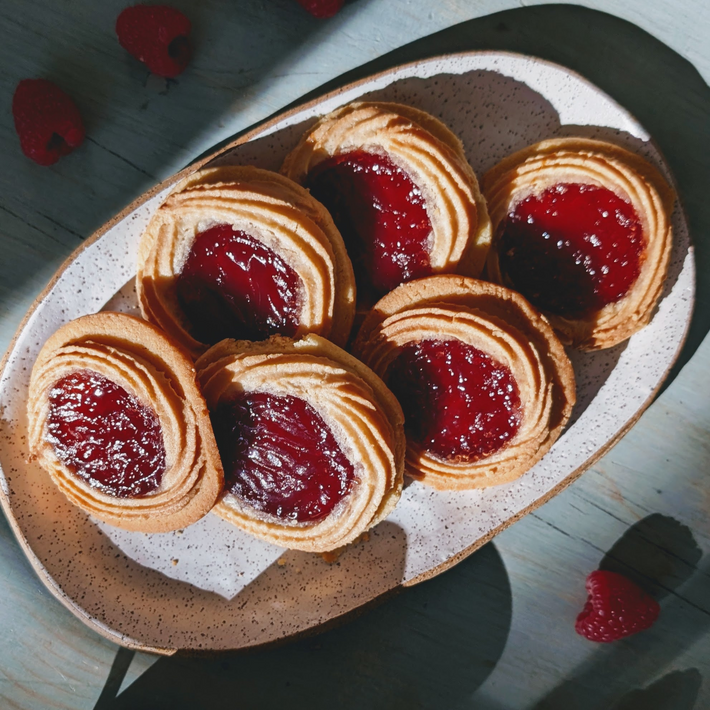 Round shortbread cookies with red raspberry jam centers arranged on a speckled oval plate