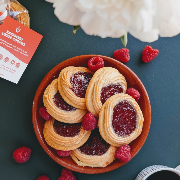 Bowl of RASPBERRY LINZER COOKIES with jam centers and fresh raspberries on a dark table