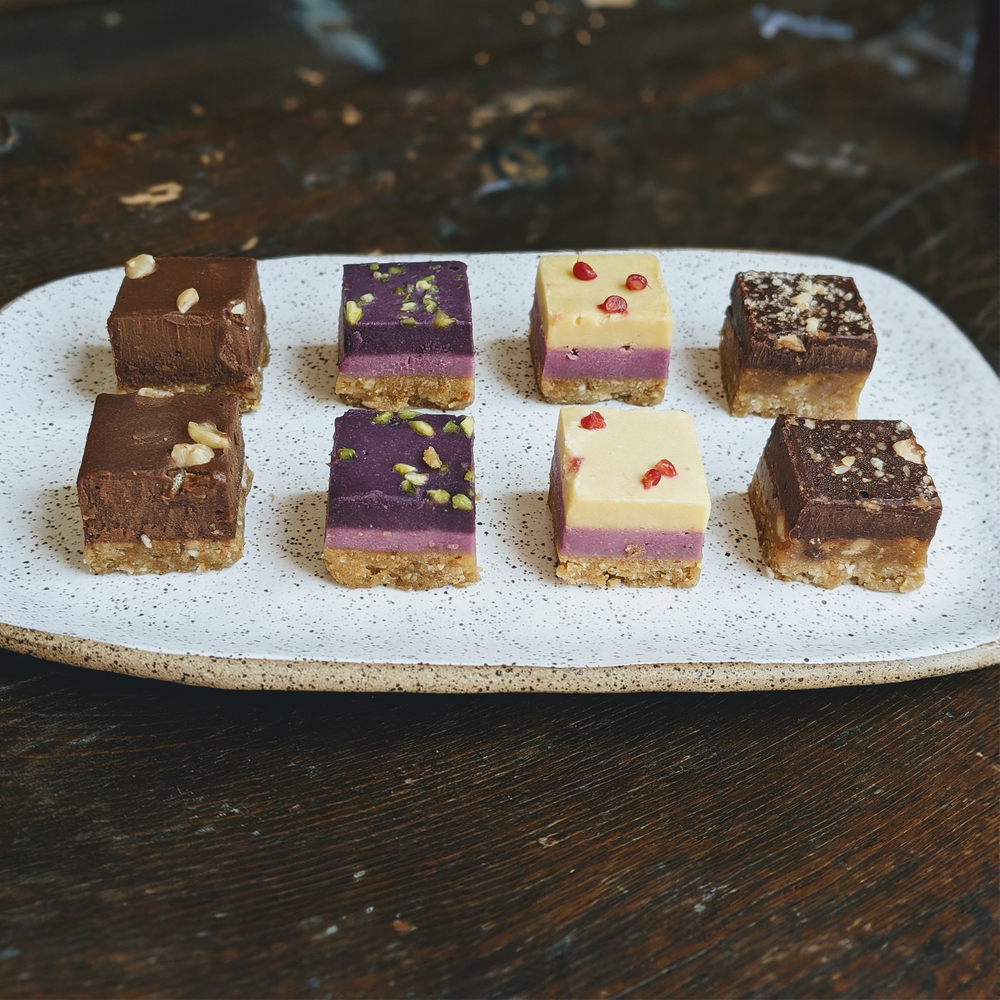 A plate of Mini Layer Cakes featuring chocolate, purple, and vanilla layers, topped with nuts and berries.