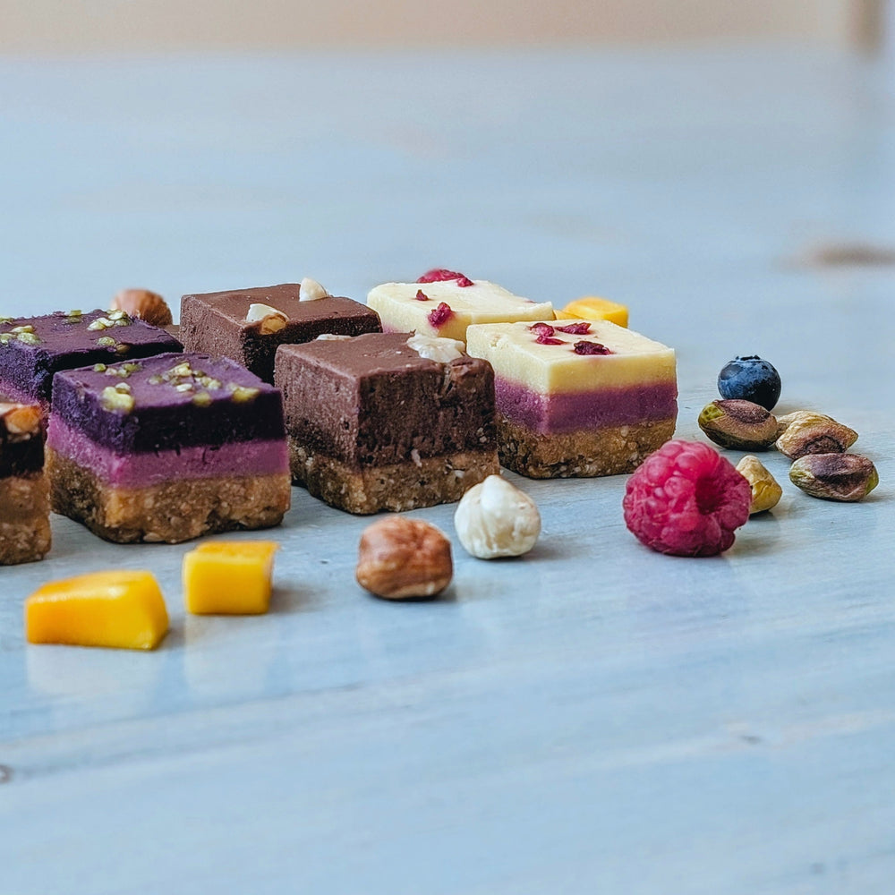 Square layered dessert bars with nut crust, purple fruit layer and chocolate or white topping, raspberry and pistachios.