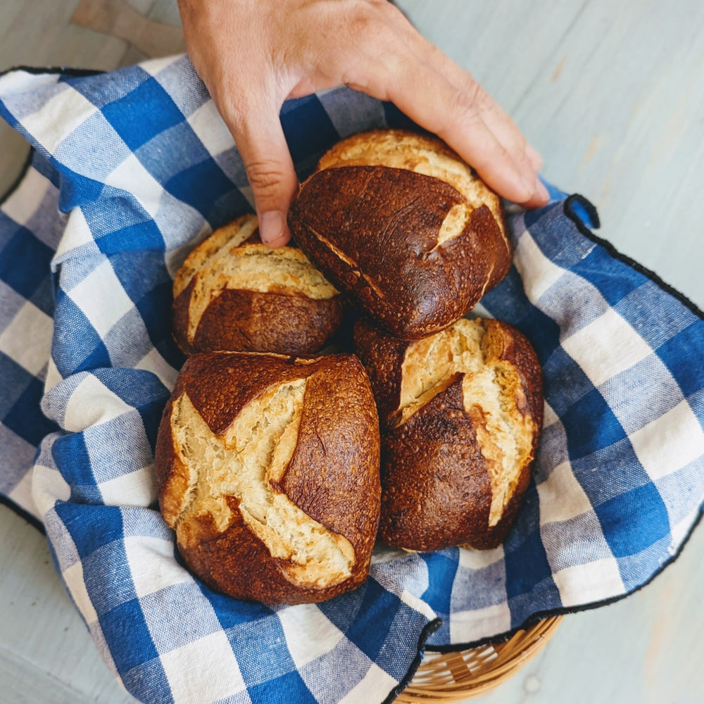 A hand holding four Bavarian pretzel buns in a checkered cloth basket.