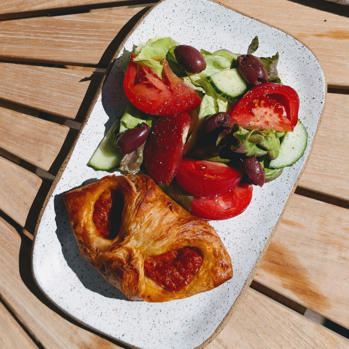 Top-down view of a Tomato Parmesan croissant showcasing golden flaky crust and tomato-parmesan filling on a speckled plate