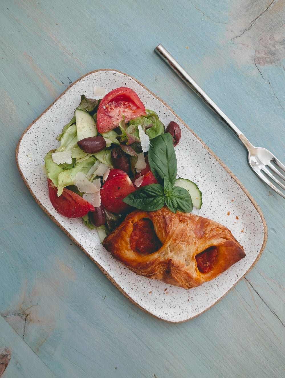 Overhead of Tomato Parmesan croissant showing tomato filling and shaved Parmesan on a speckled plate with salad and fork