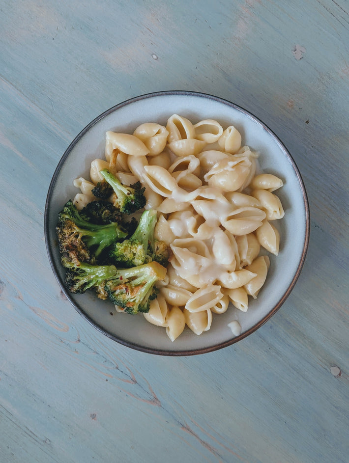 Creamy pasta shells with roasted broccoli in a bowl on a light blue wooden surface.