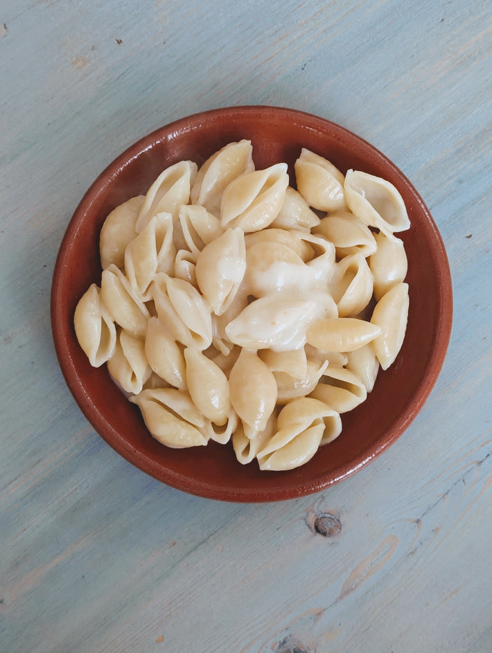 Bowl of cooked pasta shells on a light blue surface, ideal for pairing with sauces.
