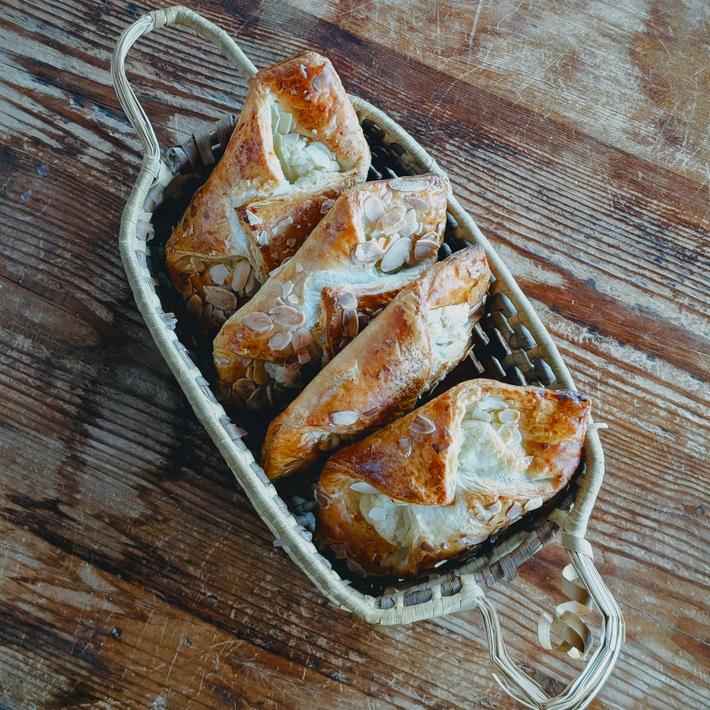 Overhead view of Almond Croissants (4-pack) showcasing almond-topped flaky pastries in a woven basket on a wooden table