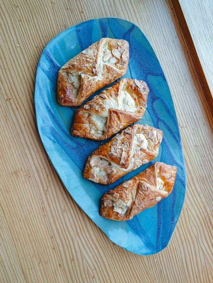 Four almond-topped cream cheese Danish pastries on an elongated blue ceramic platter on a wooden table