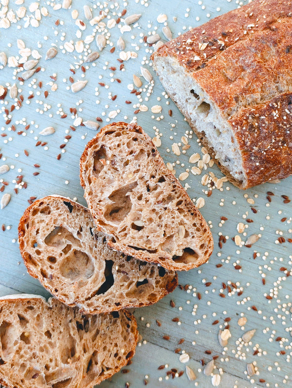 Sliced multigrain loaf with airy crumb and scattered seeds and oats on a blue wooden board.