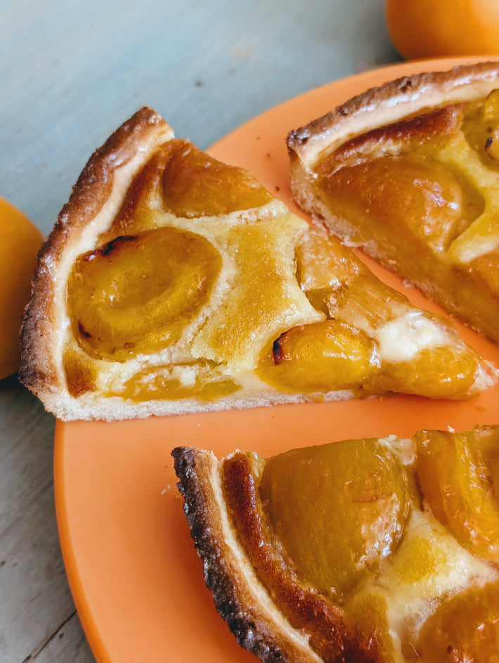 Two slices of apricot tart with glazed apricot halves on an orange plate