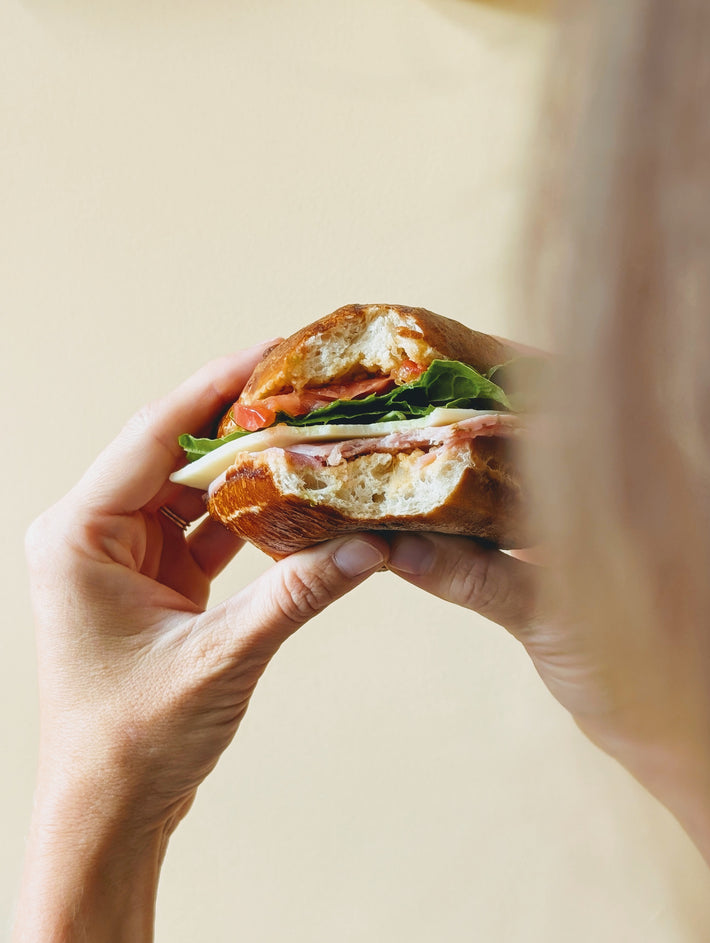 Bavarian Pretzel Bun sandwich with lettuce, tomato, and meat held by a person.