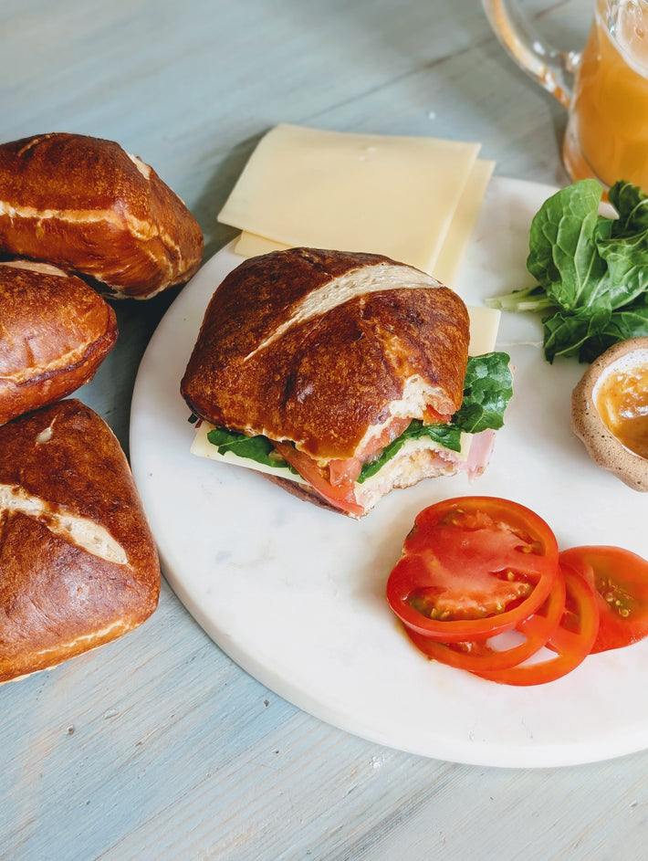 Bavarian pretzel sandwich with greens, tomato, cheese, and sliced tomatoes on a plate.