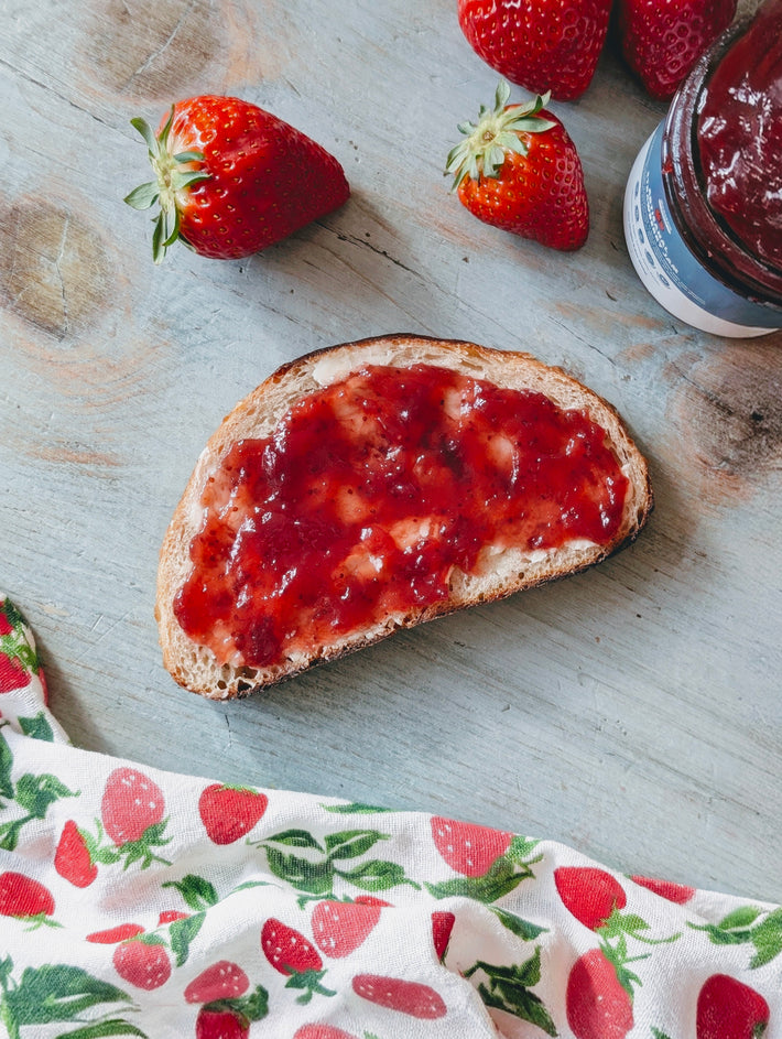 Toasted bread slice spread with strawberry jam on a wooden board, with fresh strawberries, jam jar and strawberry cloth.