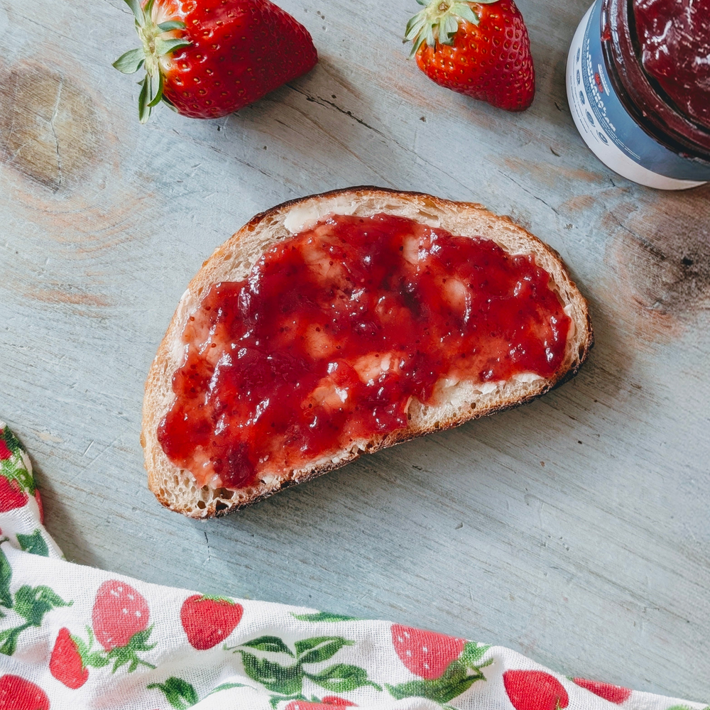 Toast with strawberry jam on a wooden surface with strawberries and a jar of jam.