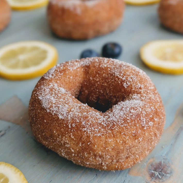 Close-up of blueberry-lemon donut showcasing a sugar-dusted golden exterior with lemon slices and blueberries on a light-blue wooden board