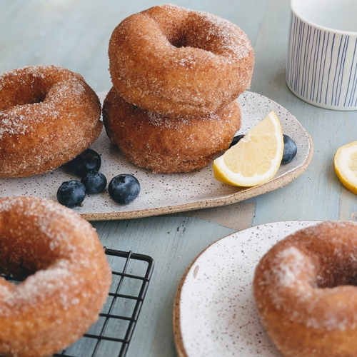 Three-quarter view of Blueberry Lemon donuts showcasing sugar-coated surface, blueberries, and a lemon wedge on a light blue table