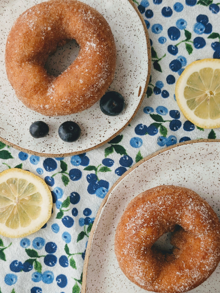 Overhead view of Blueberry Lemon donuts with sugar coating on speckled plates with blueberries and lemon slices