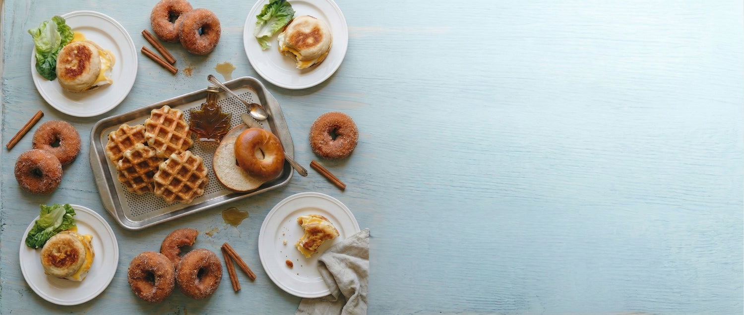 Assorted breakfast items including waffles, donuts, and pastries on a light blue background.