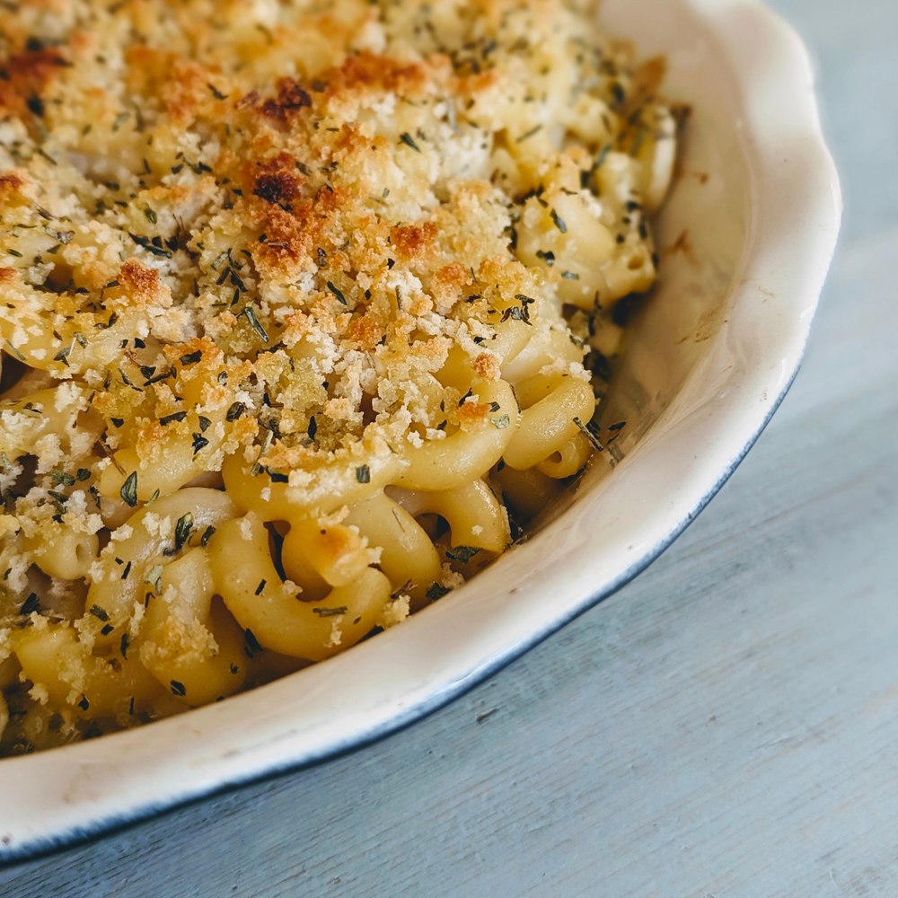 Baked macaroni and cheese with golden breadcrumb and herb topping in a white ceramic baking dish, corner close-up