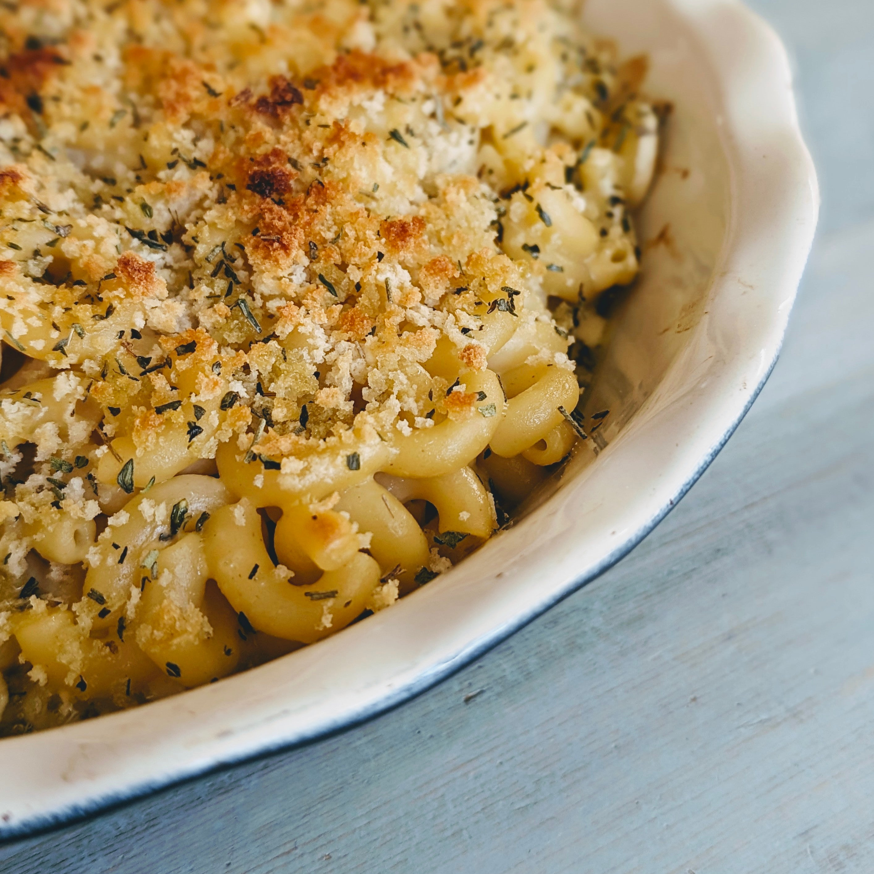 Baked macaroni and cheese with golden breadcrumb and herb topping in a white ceramic baking dish, corner close-up