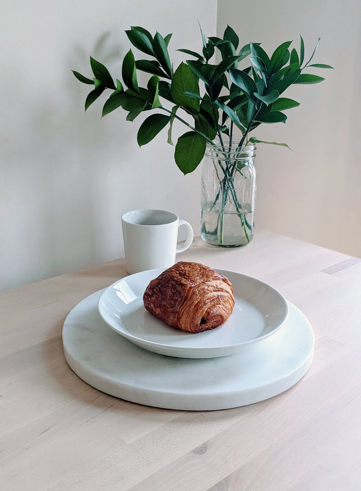 A chocolate croissant on a plate with a vase of leaves in the background