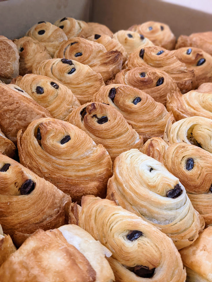 A close-up of assorted flaky pastries, including chocolate croissants, arranged in a box.