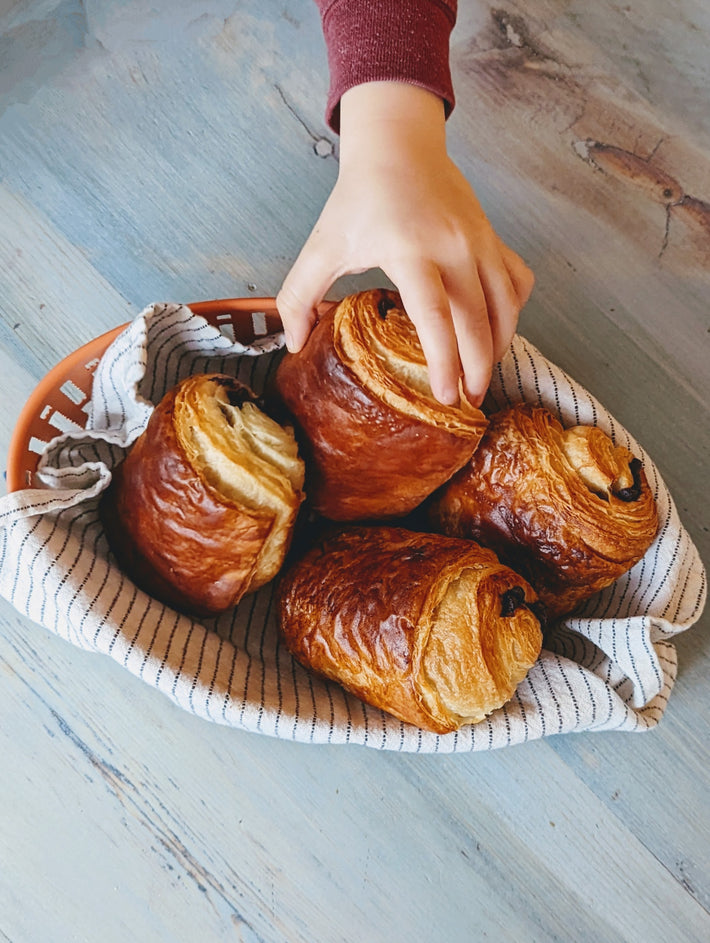 A hand reaching for freshly baked croissants in a basket lined with a striped cloth.