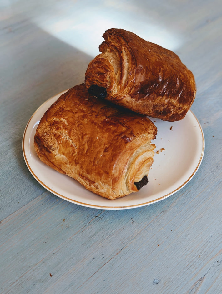 Two flaky chocolate croissants on a white plate