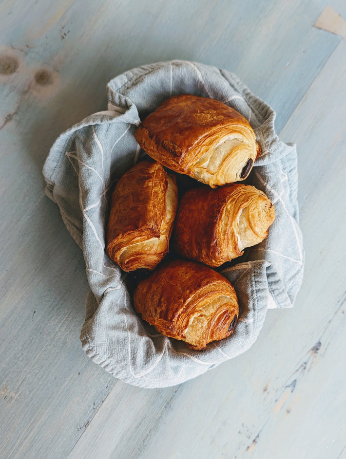 Four golden-brown chocolate croissants in a cloth-lined basket