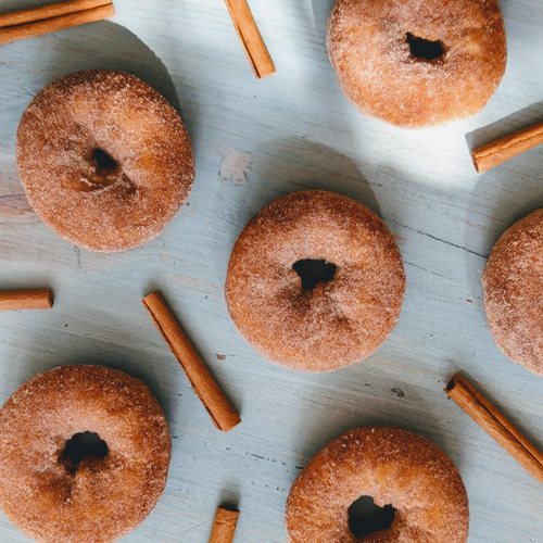 Cinnamon-sugar donuts and cinnamon sticks arranged on a pale wooden surface