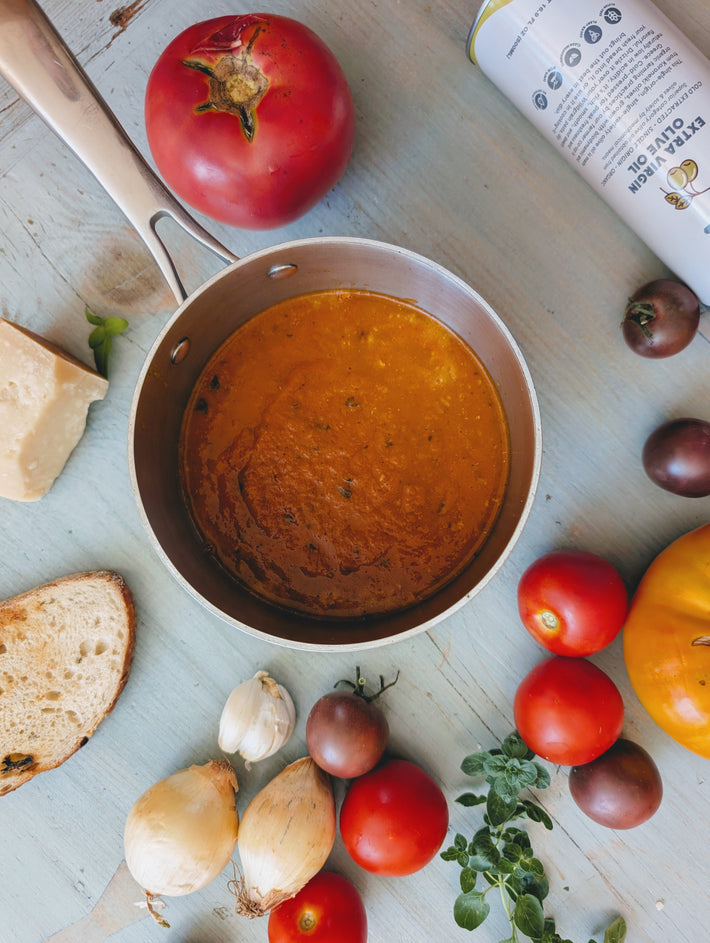 Pot of soup with tomatoes, bread, and herbs on a wooden surface