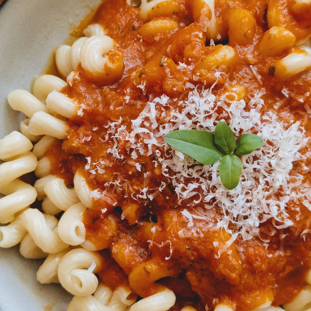 Cavatappi pasta with tomato sauce, grated Parmesan and a small basil sprig, close-up