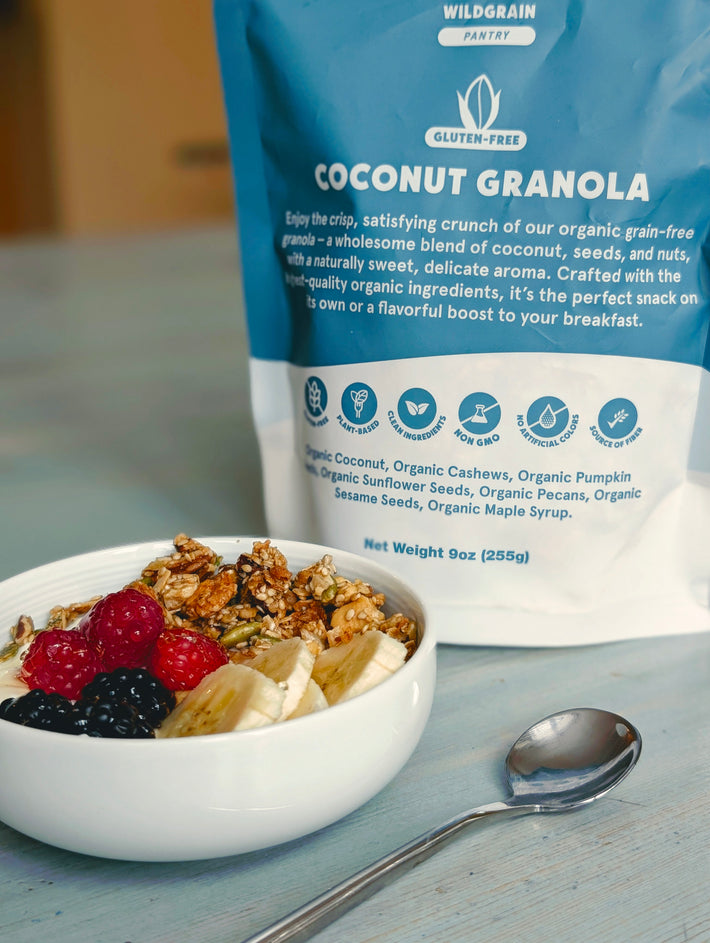 Front of 9 ounce Coconut Granola bag showing label and icons with bowl of granola topped with banana and berries on table
