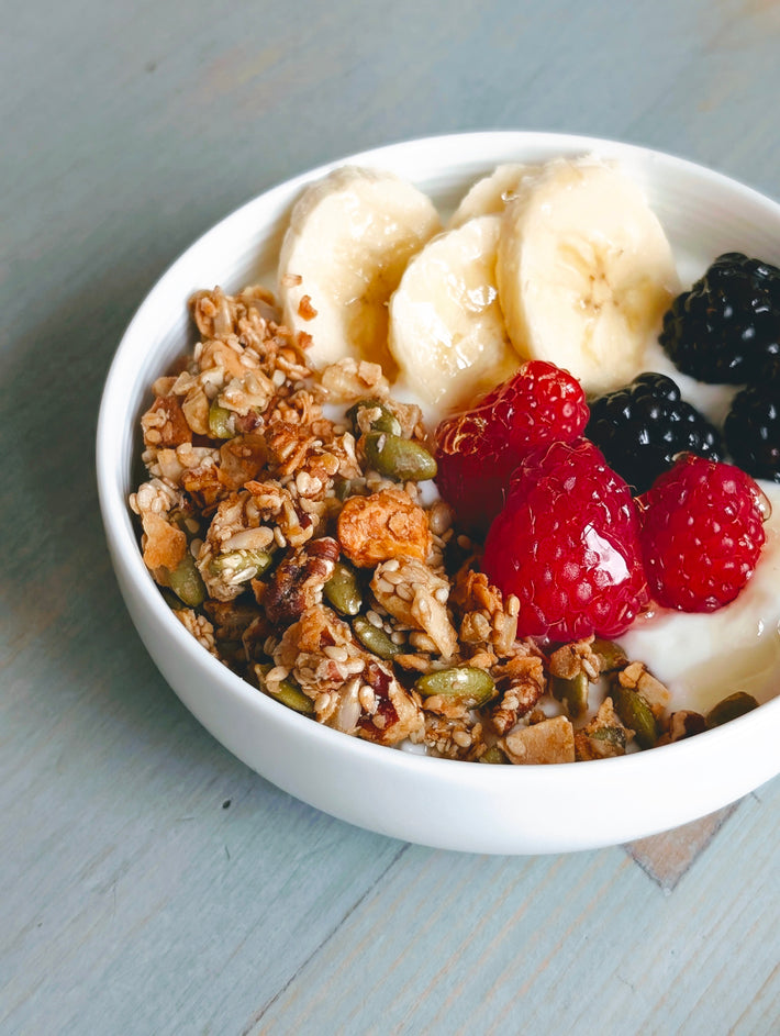 Three-quarter view of Gluten-Free Coconut Granola in a white bowl showcasing oat clusters and seeds with banana slices and berries
