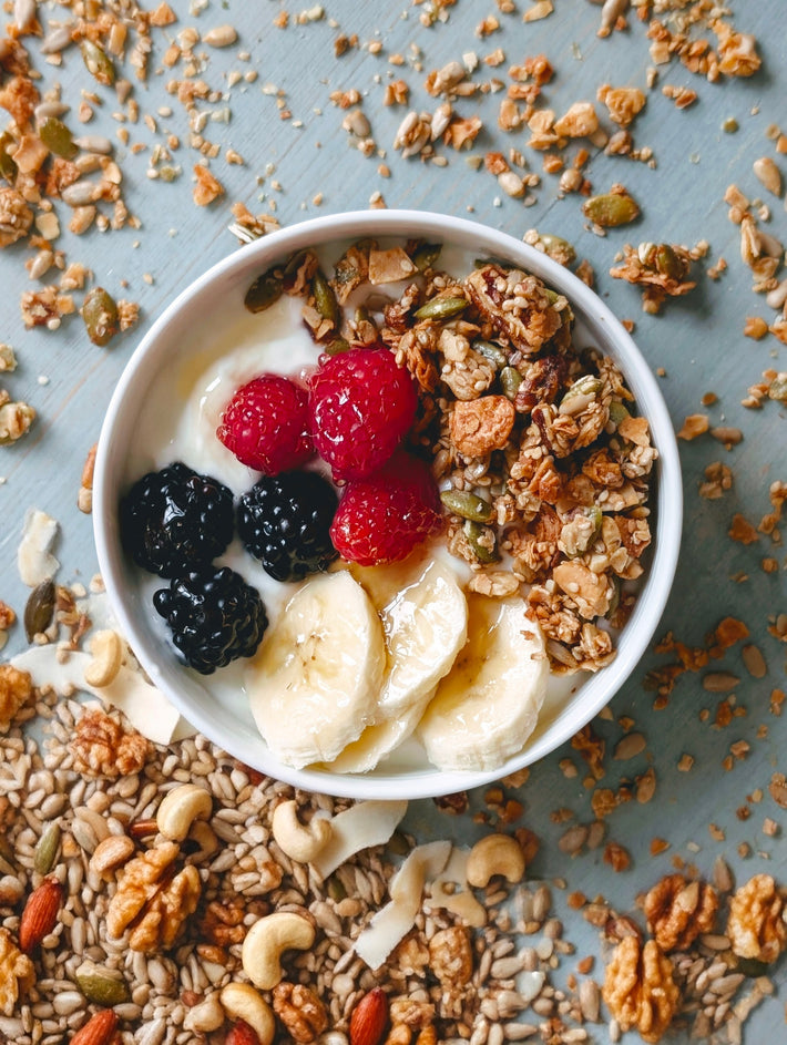 Bowl of gluten-free coconut granola with yogurt, banana slices, raspberries and blackberries on a gray table