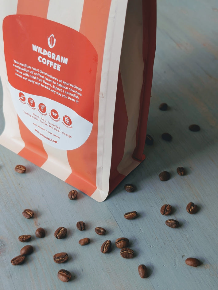 Angled close-up of Wildgrain Coffee whole-bean medium roast bag with front label and beans on light blue surface
