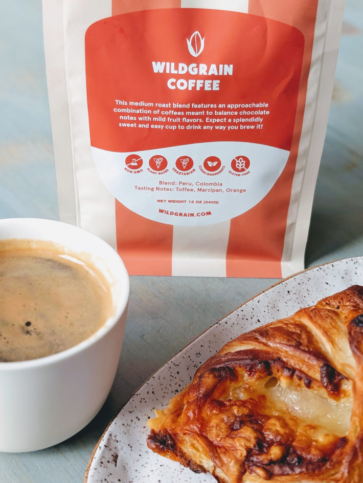 Wildgrain whole bean coffee bag with orange-and-white label WILDGRAIN COFFEE, cup of coffee and pastry