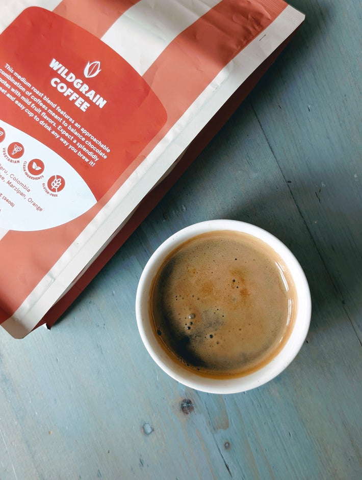 Top-down view of Wildgrain Blend medium-roast whole bean coffee bag and cup of brewed coffee on a light blue wooden table