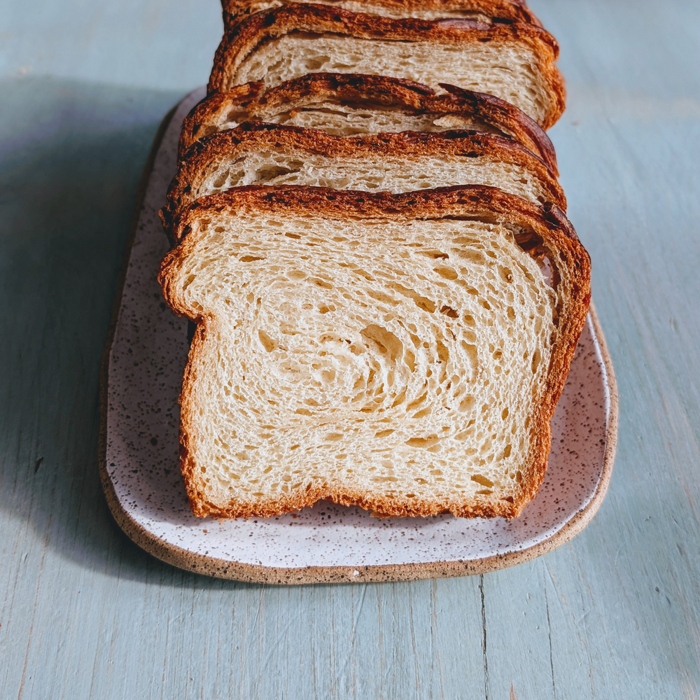 Sliced swirled white bread on a speckled ceramic plate set on a pale blue wooden table.