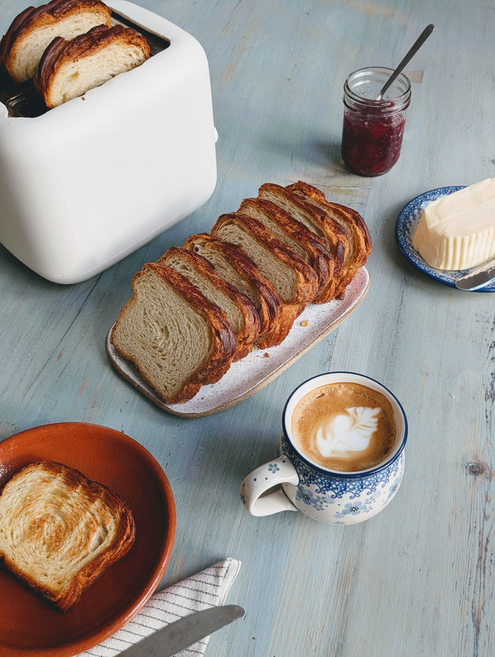 A cozy breakfast scene with sliced bread, coffee with latte art, butter, jam, and a toaster on a wooden table.